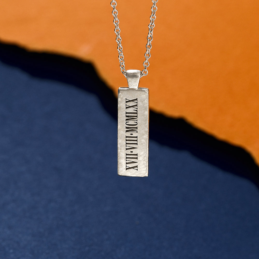 Silver pendant with Roman numerals on a blue and orange gradient background