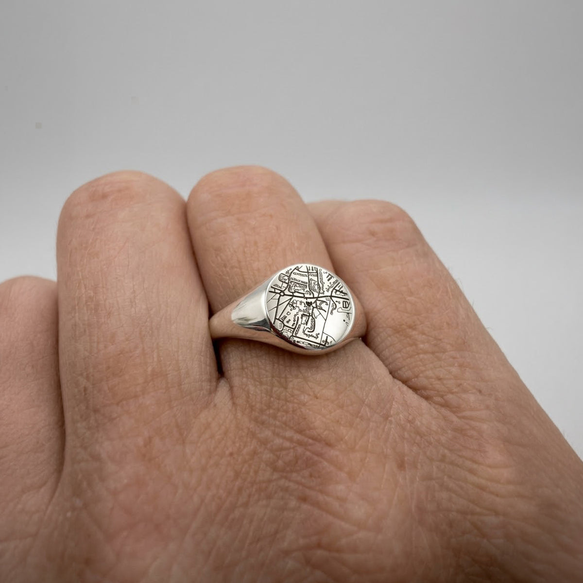 A silver signet ring with an engraved map design on the face, shown worn on a person's ring finger against a neutral gray background.