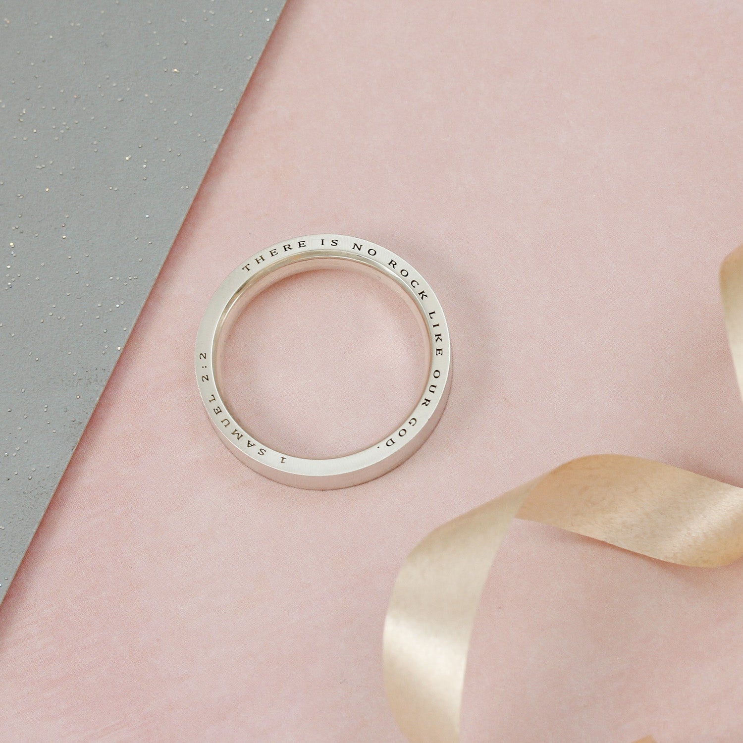 Silver ring with engraved text on a pink and gray background