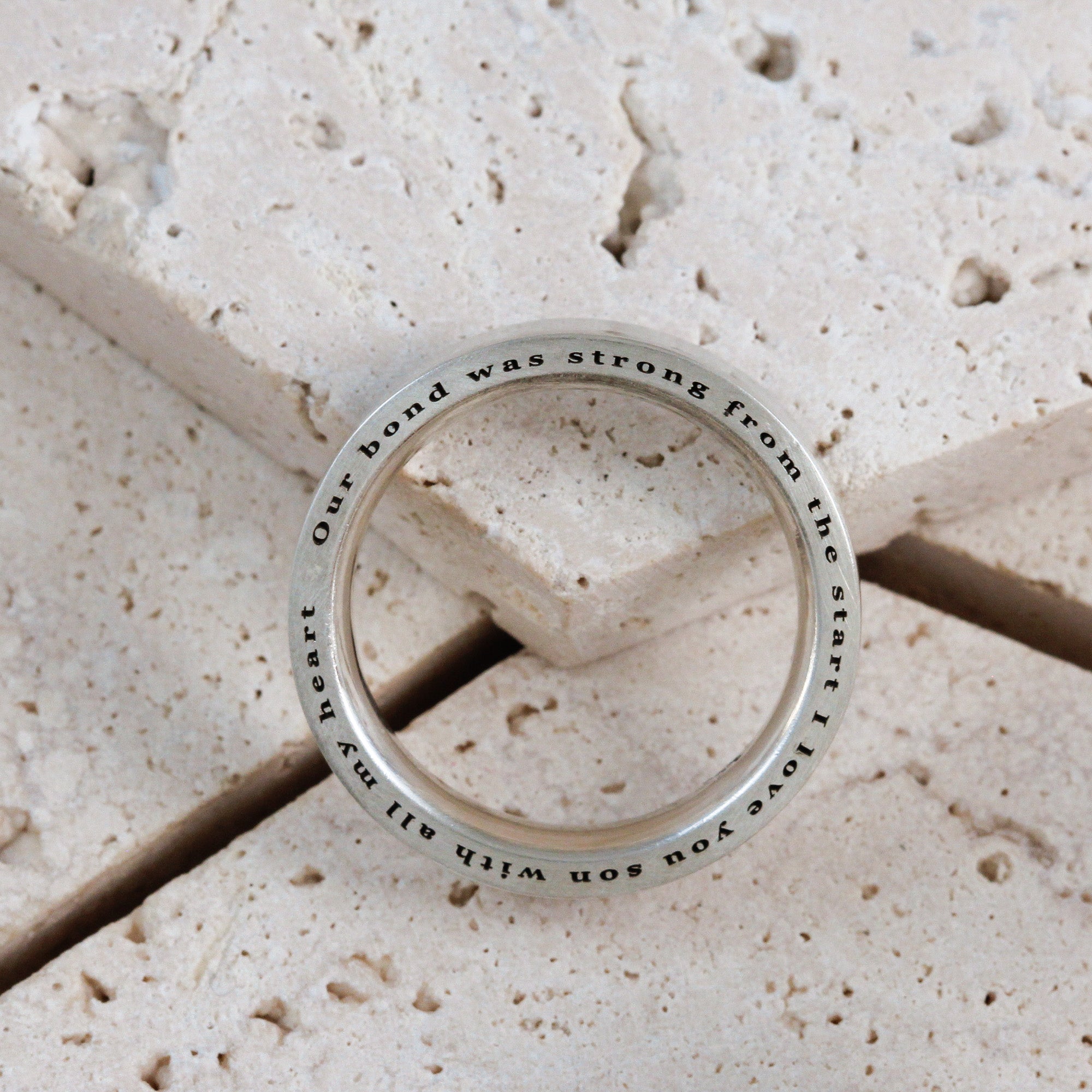 Silver ring with engraved text on a stone surface