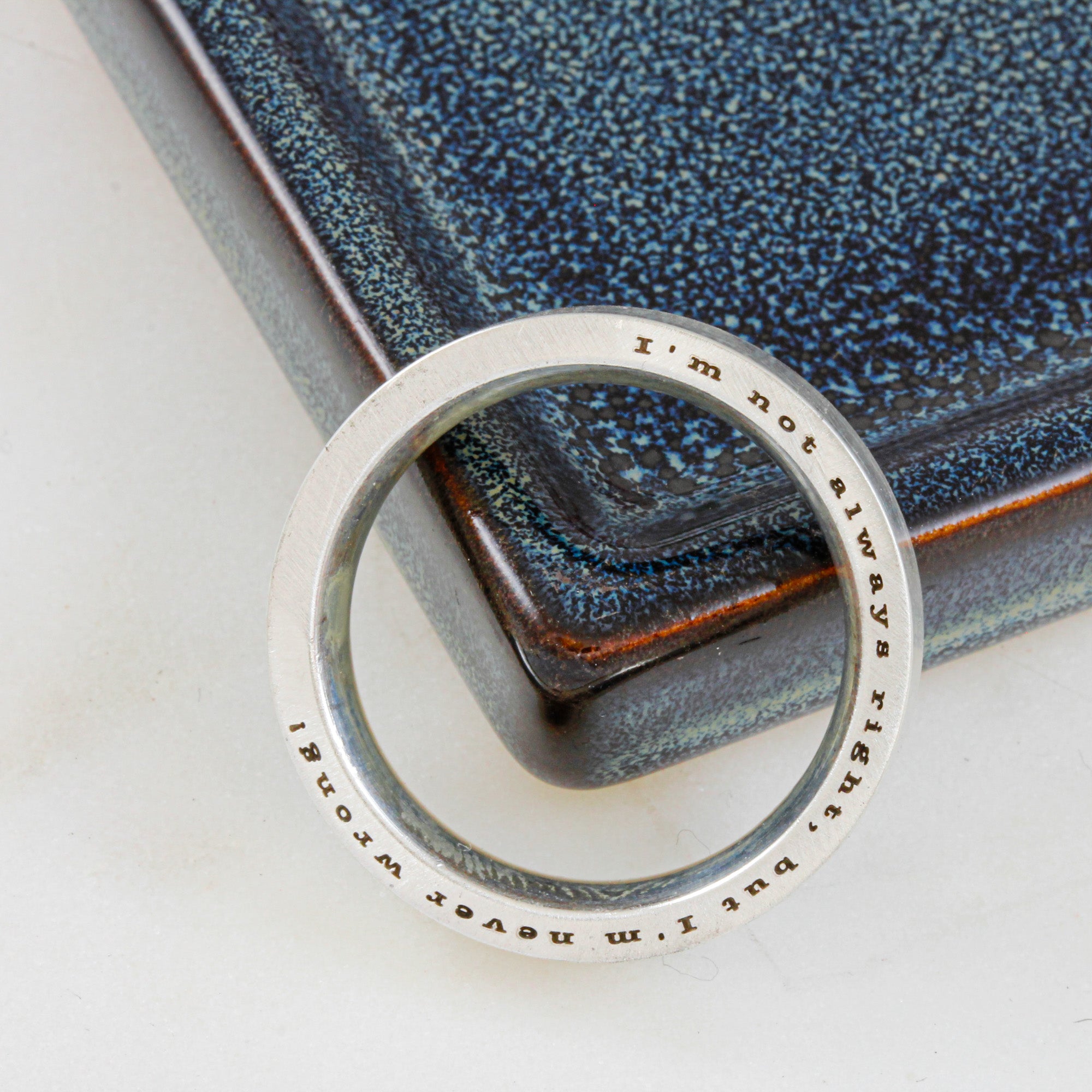 Silver ring with engraved text on a textured blue surface