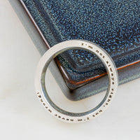 Silver ring with engraved text on a textured blue surface