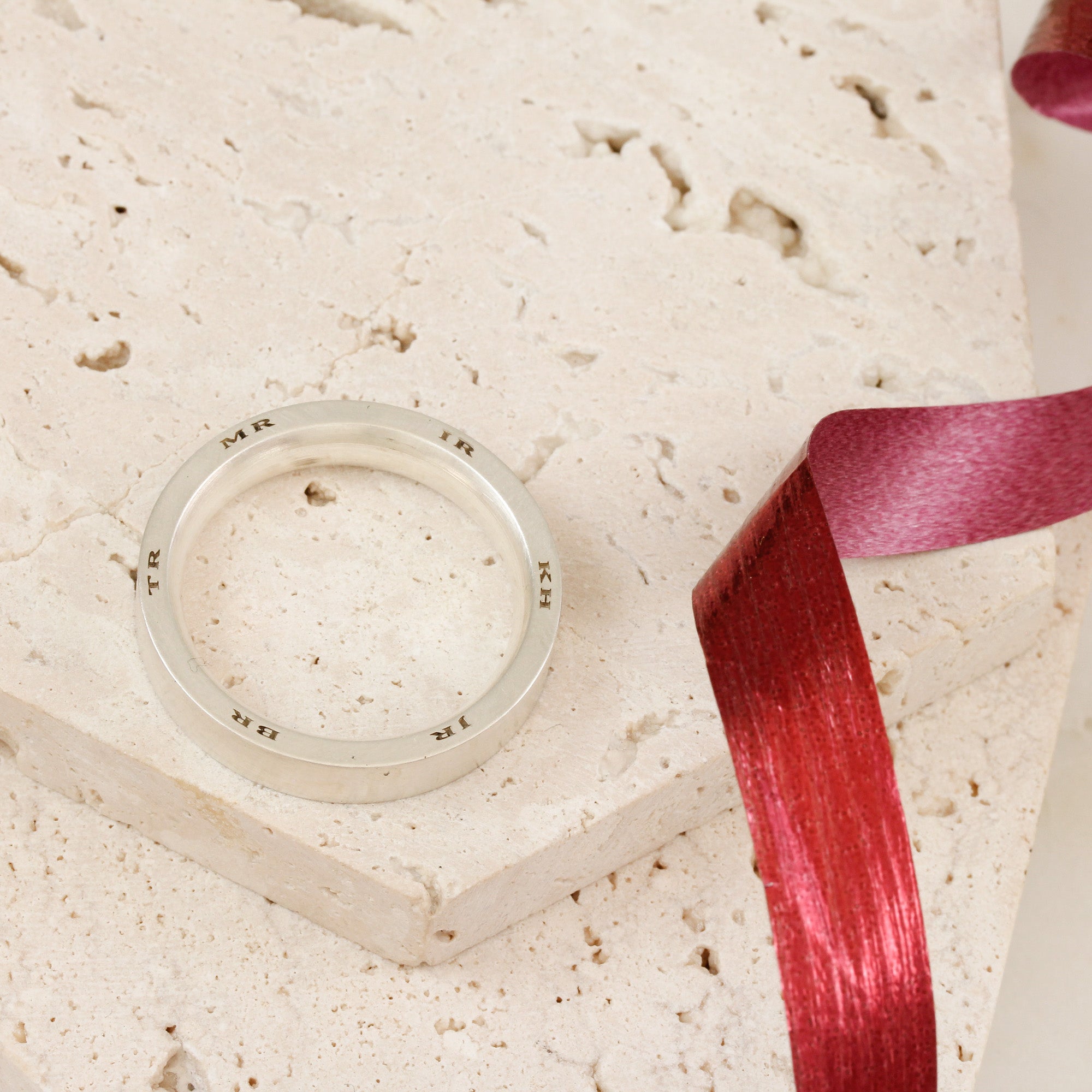 Silver ring on a textured beige surface with a red ribbon