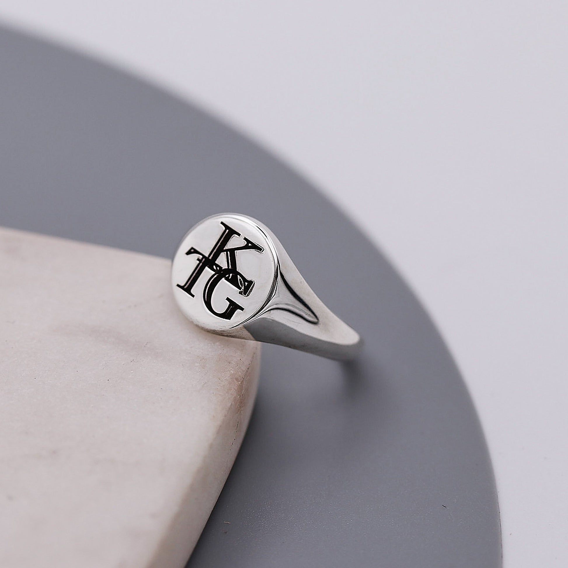 Silver ring with monogram design on a gray surface
