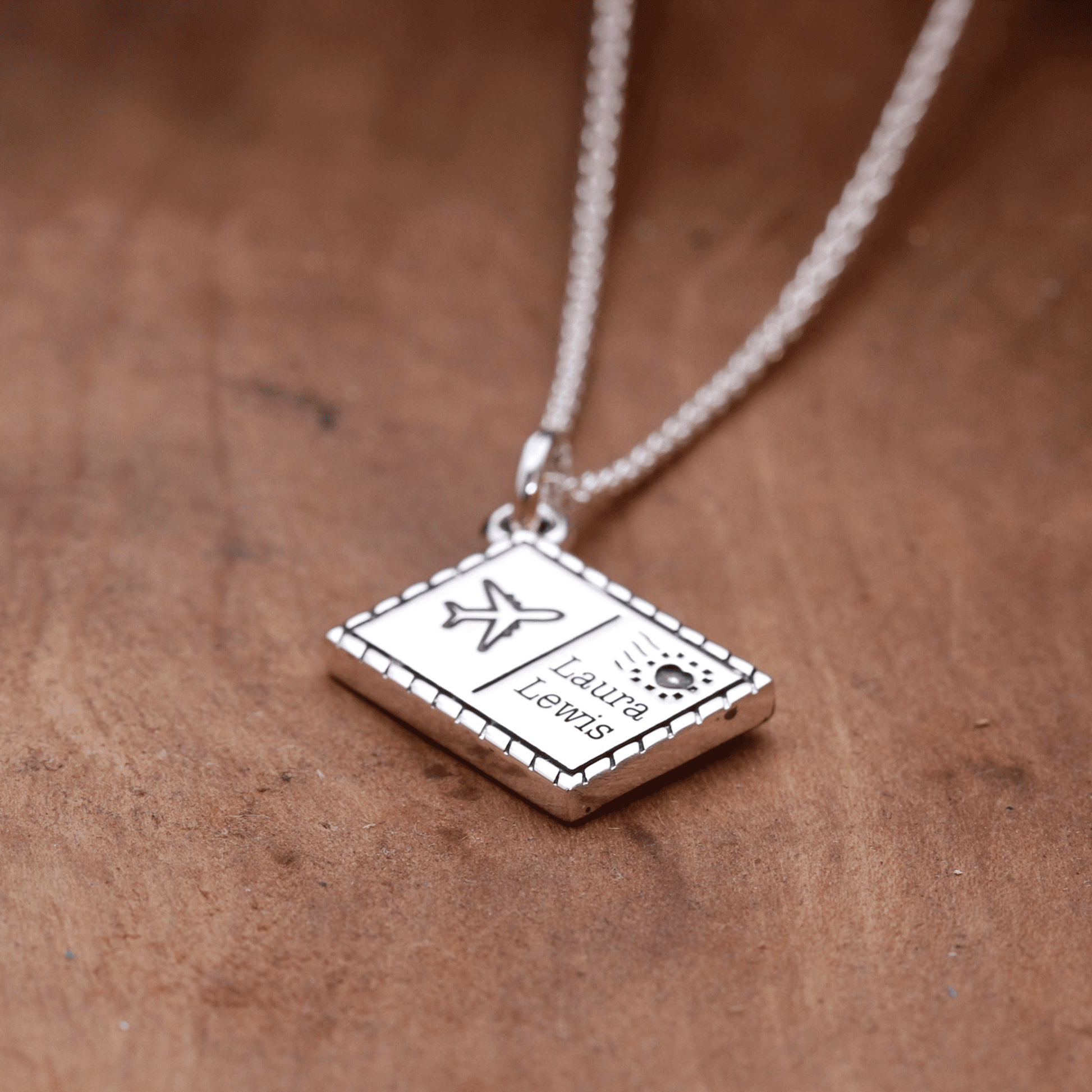 Silver postcard necklace with engraved text on a brown surface