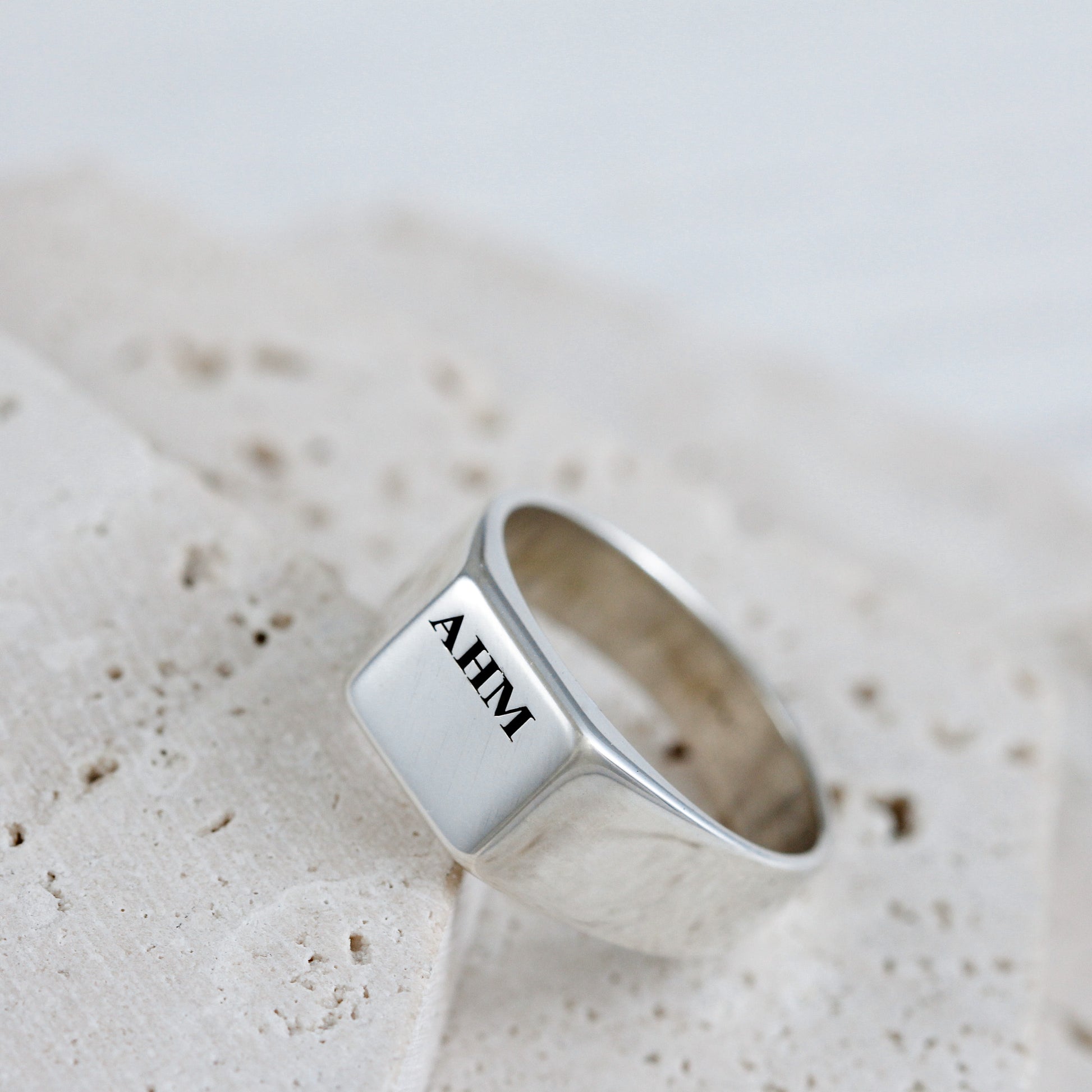 Silver ring with 'AHM' engraving on a textured beige surface