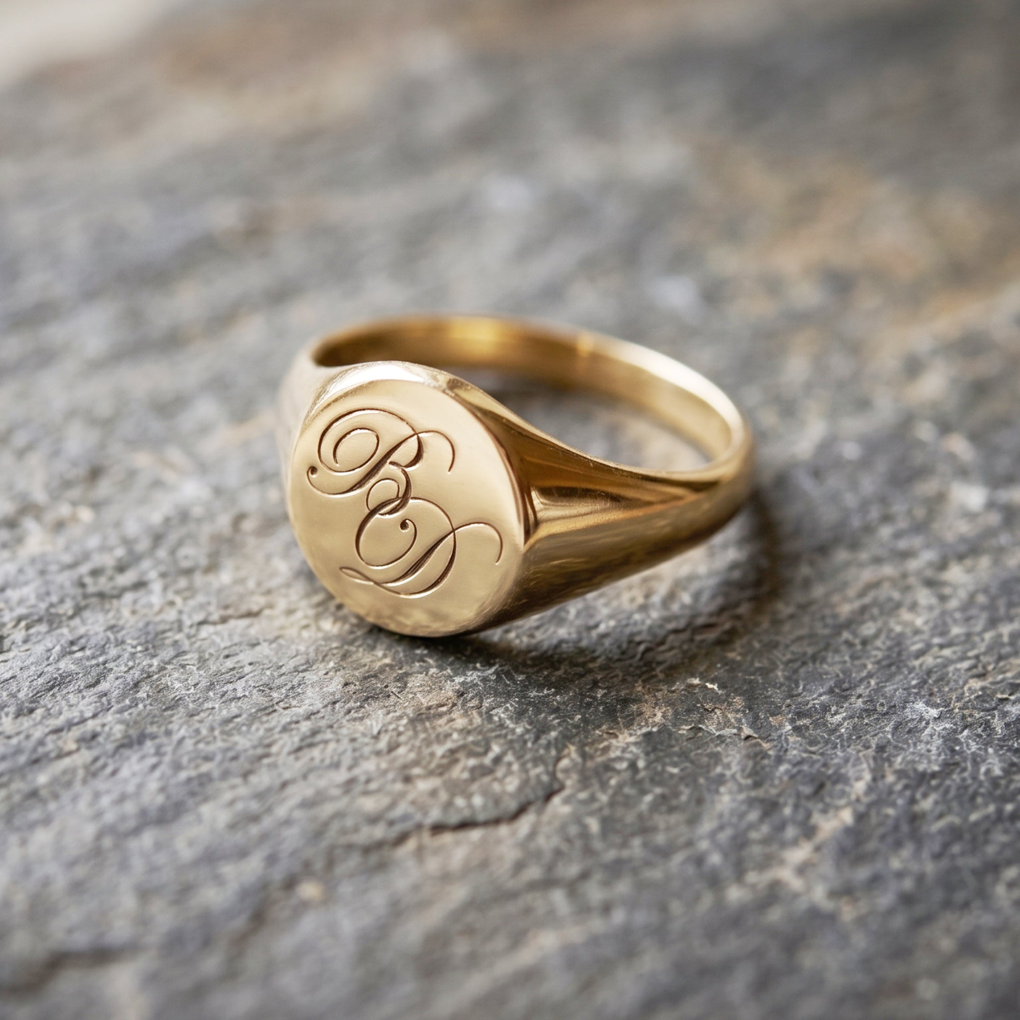 Gold ring with engraved initials on a stone surface