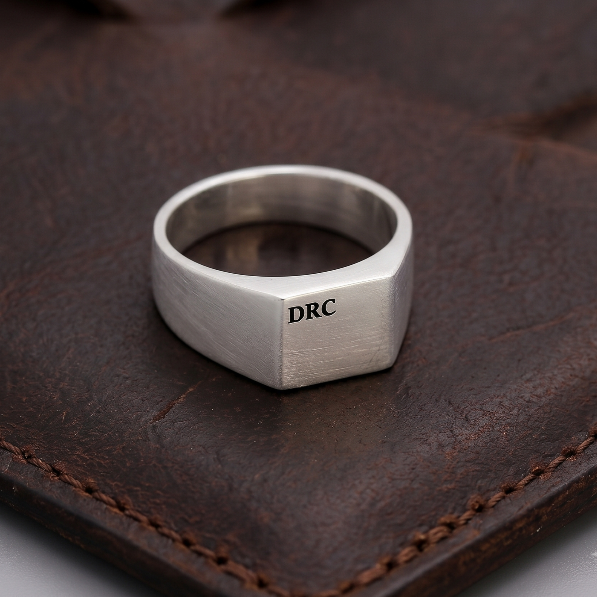 Silver ring with 'DRC' engraving on a brown leather surface