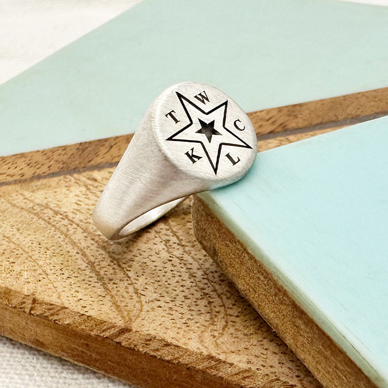 Silver ring with star design and engraved text on a wooden and stone surface