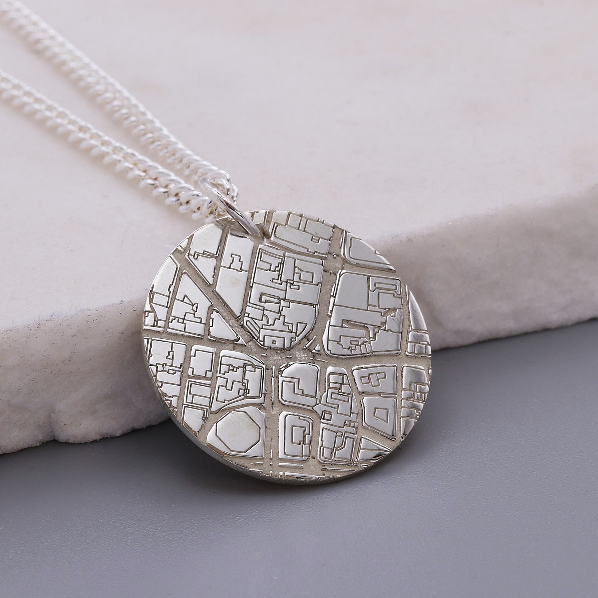Silver necklace with a detailed map pendant on a light gray surface