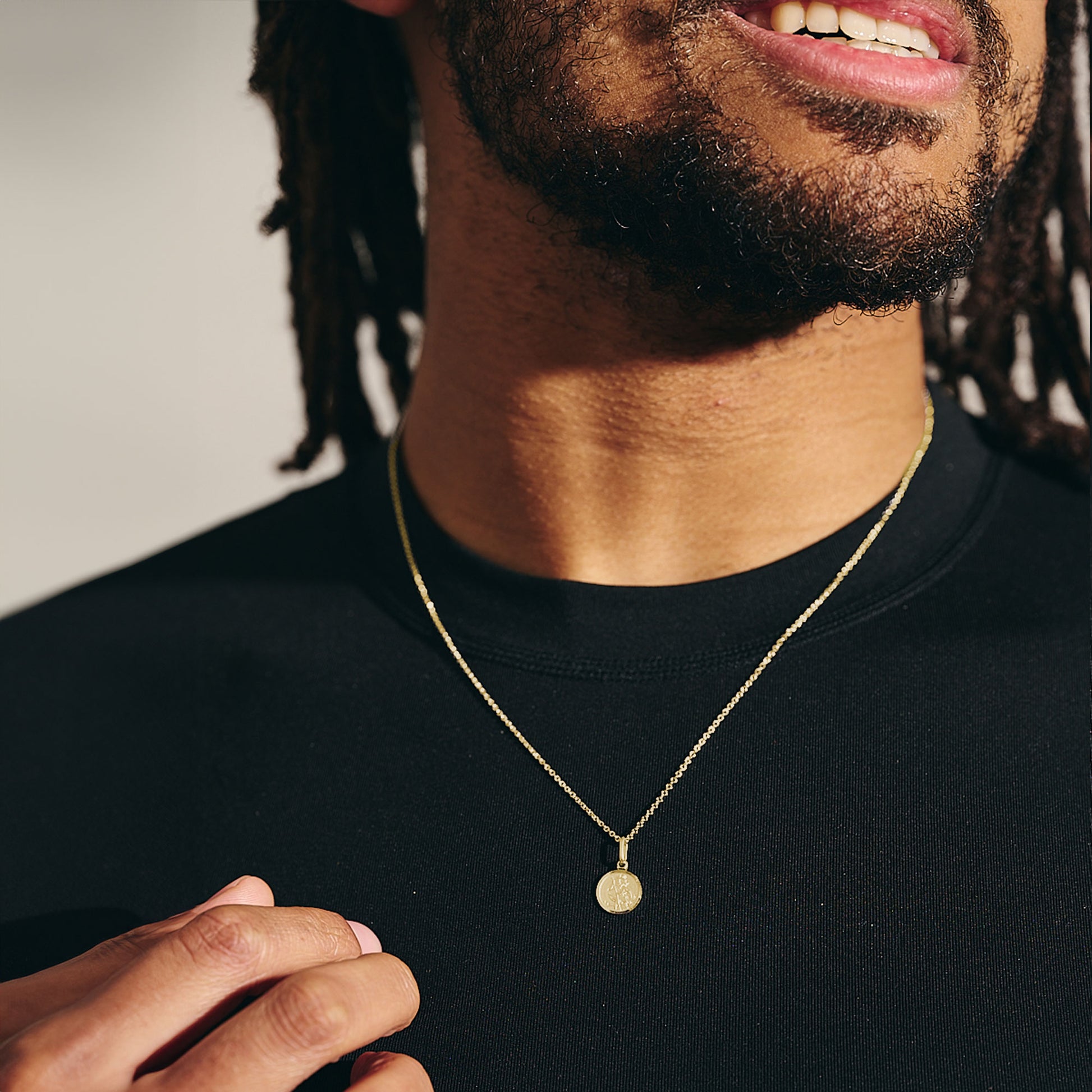 Man wearing a gold necklace with a pendant against a neutral background