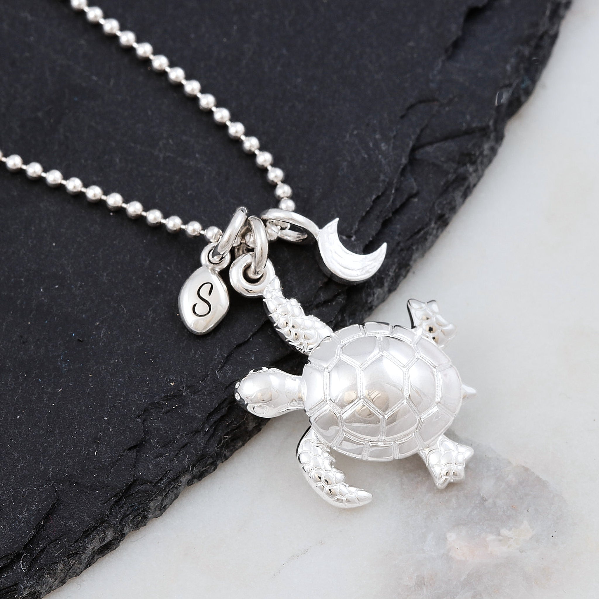 Silver turtle pendant necklace with ballc chain on a dark slate surface