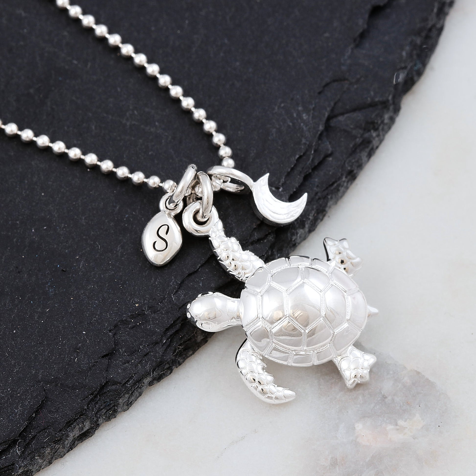 Silver turtle pendant necklace with ballc chain on a dark slate surface